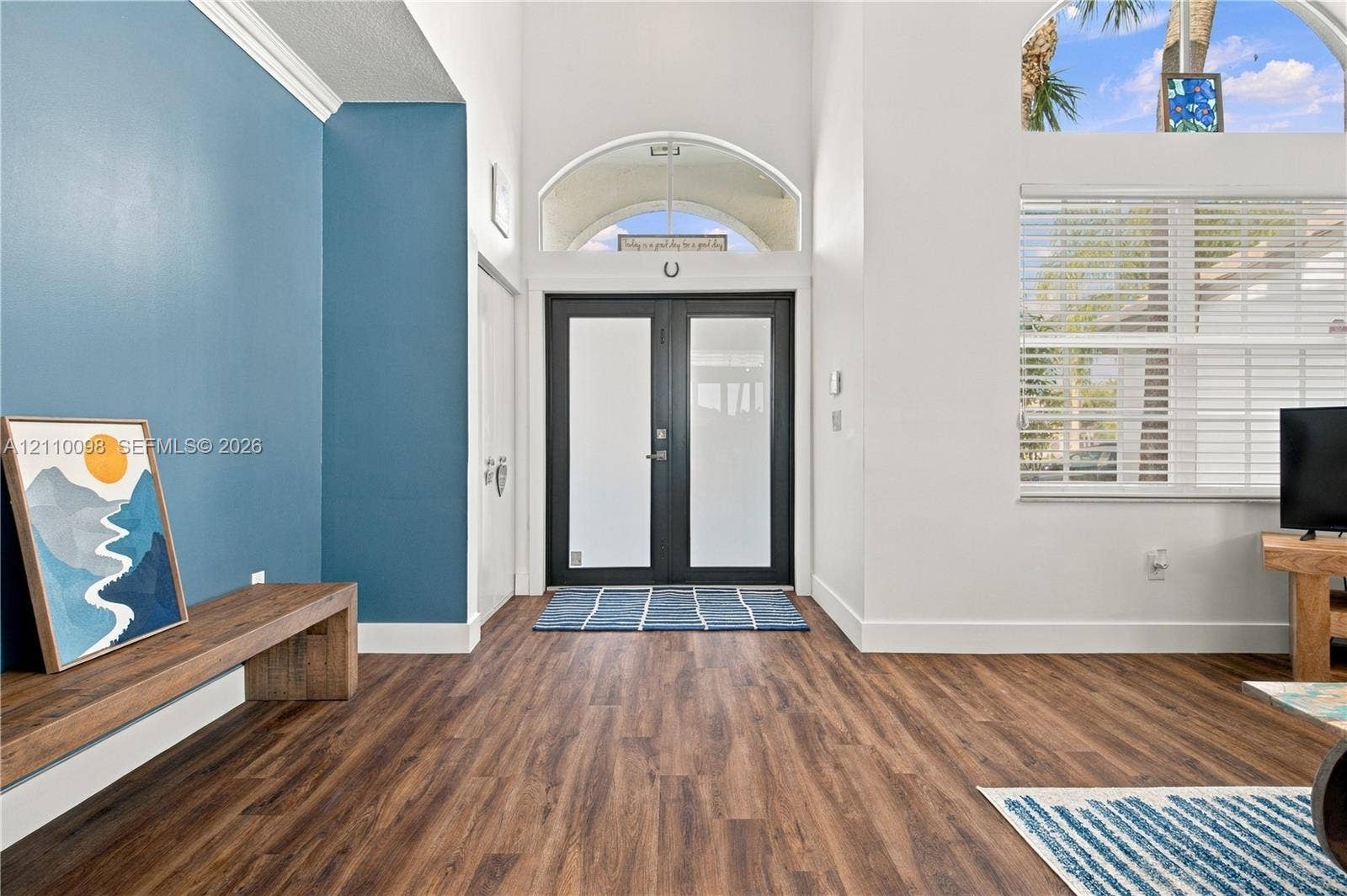 Entryway featuring double doors with frosted glass inserts, high ceilings, wood-finish flooring, and an arched transom window