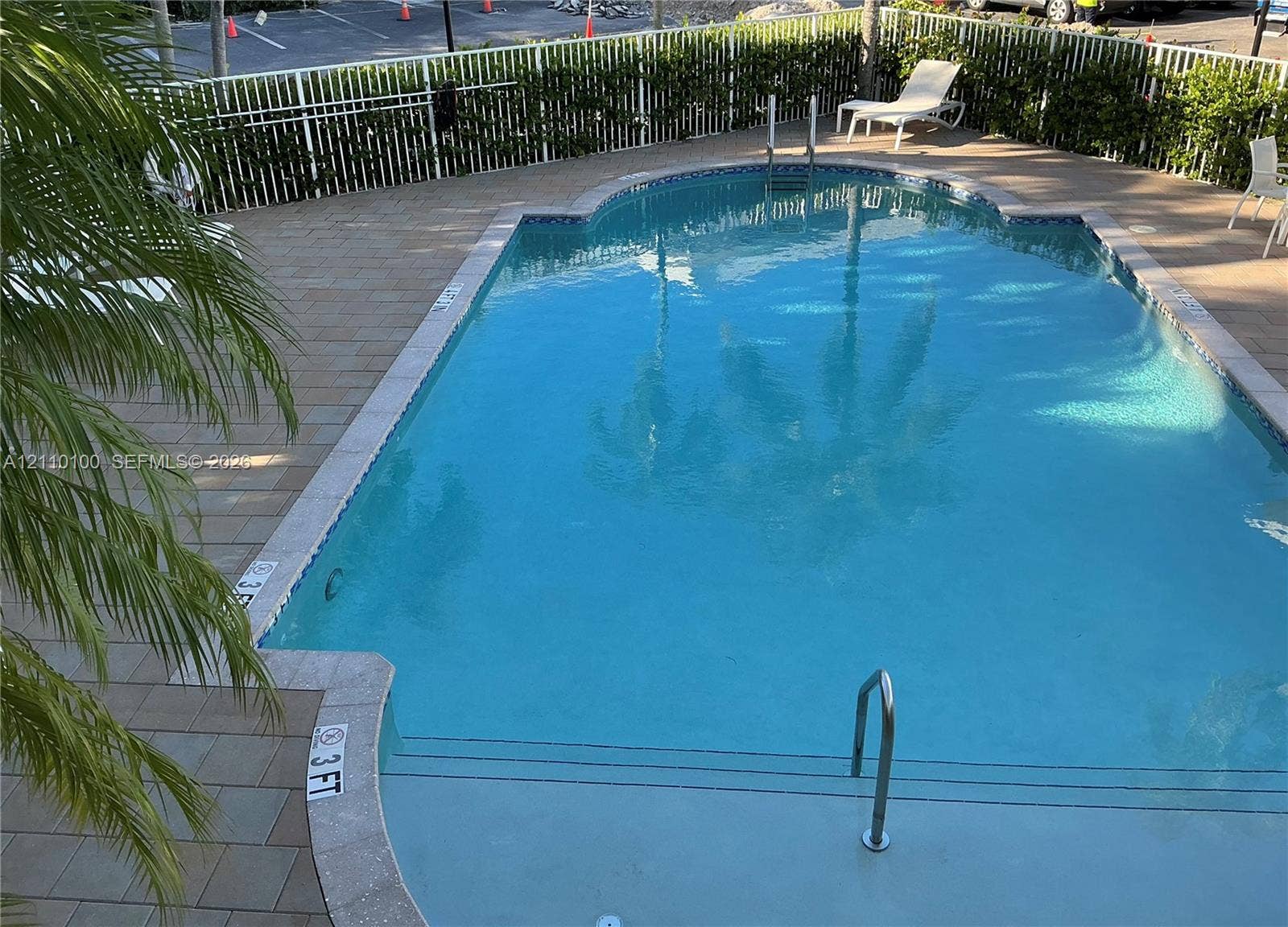 In-ground swimming pool featuring a tiled deck, decorative pool coping, metal handrails, and a perimeter fence