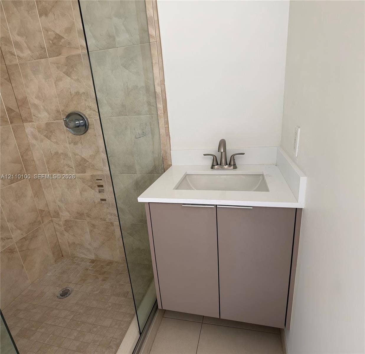 Floating vanity with a light-toned solid surface countertop, undermount sink, brushed nickel faucet, and a walk-in shower featuring glass enclosure and full-height stone-finish wall tile
