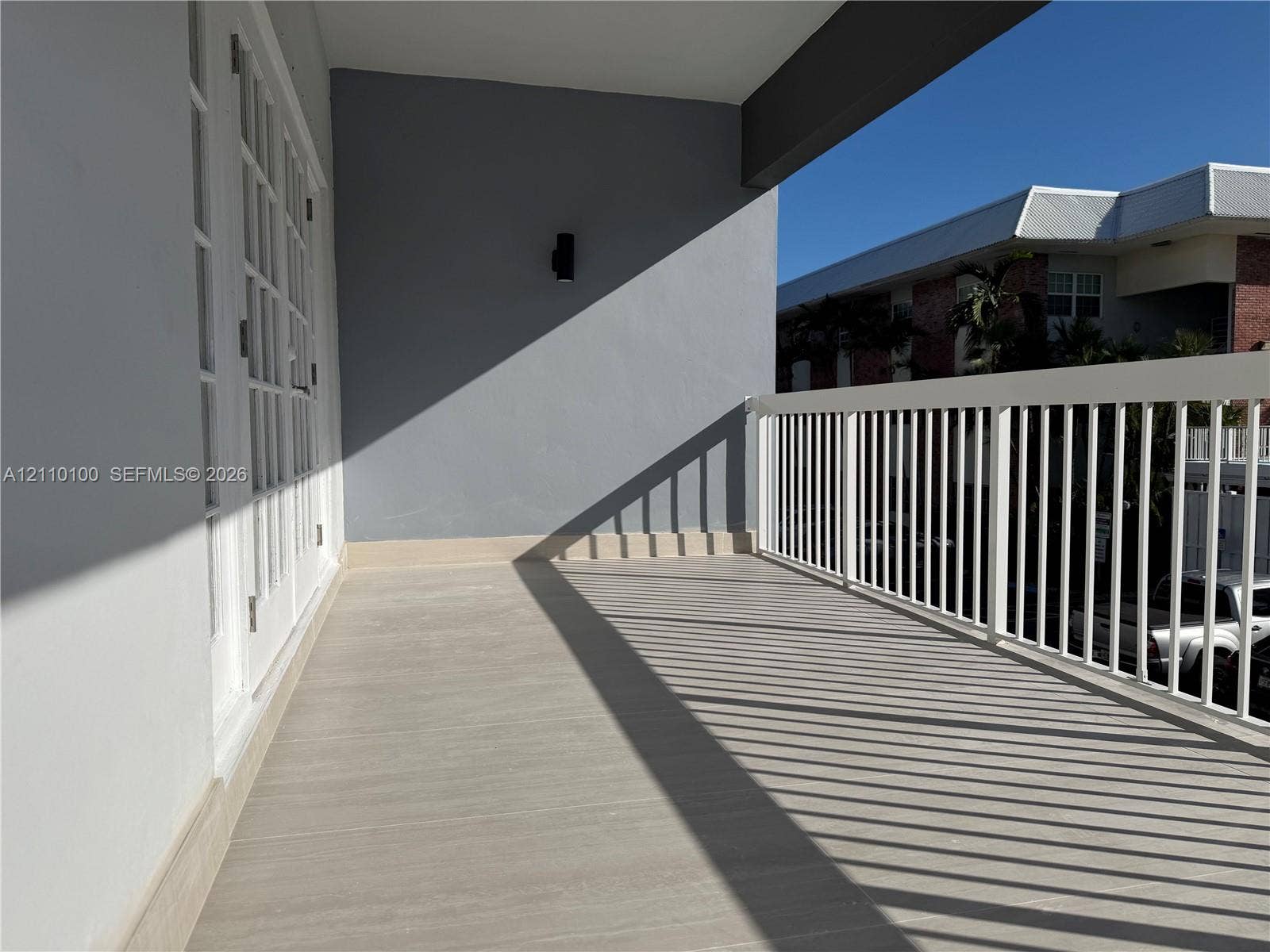 Covered balcony featuring wood-finish flooring, white vertical-slat railings, multi-pane glass doors, and wall-mounted exterior lighting