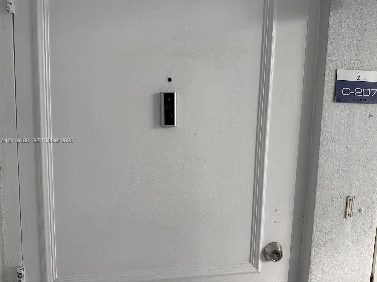 White paneled entry door equipped with a mounted smart doorbell and circular deadbolt lock