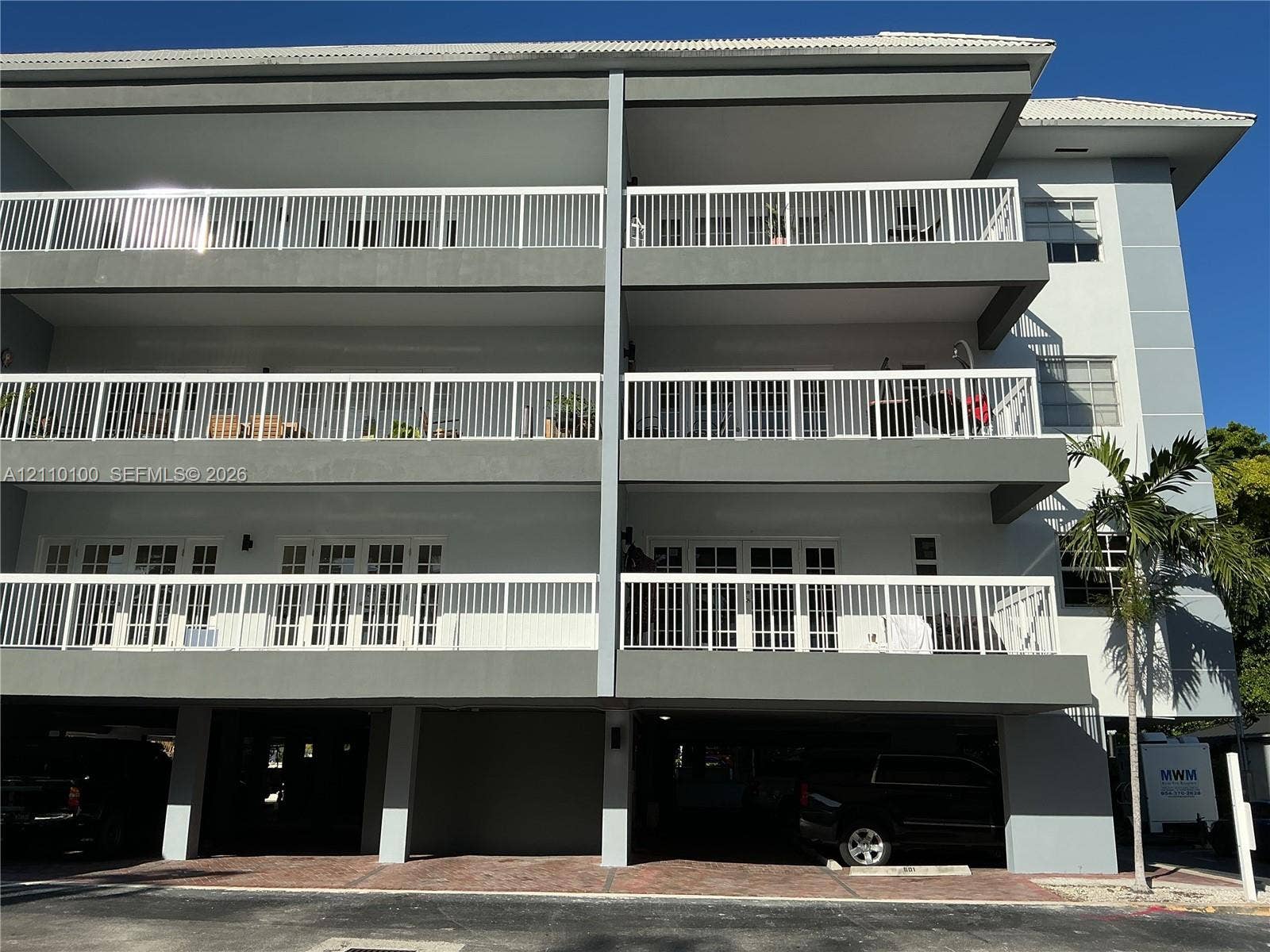 Multi-story exterior featuring multi-level balconies, white metal railings, French doors, and covered ground-level parking