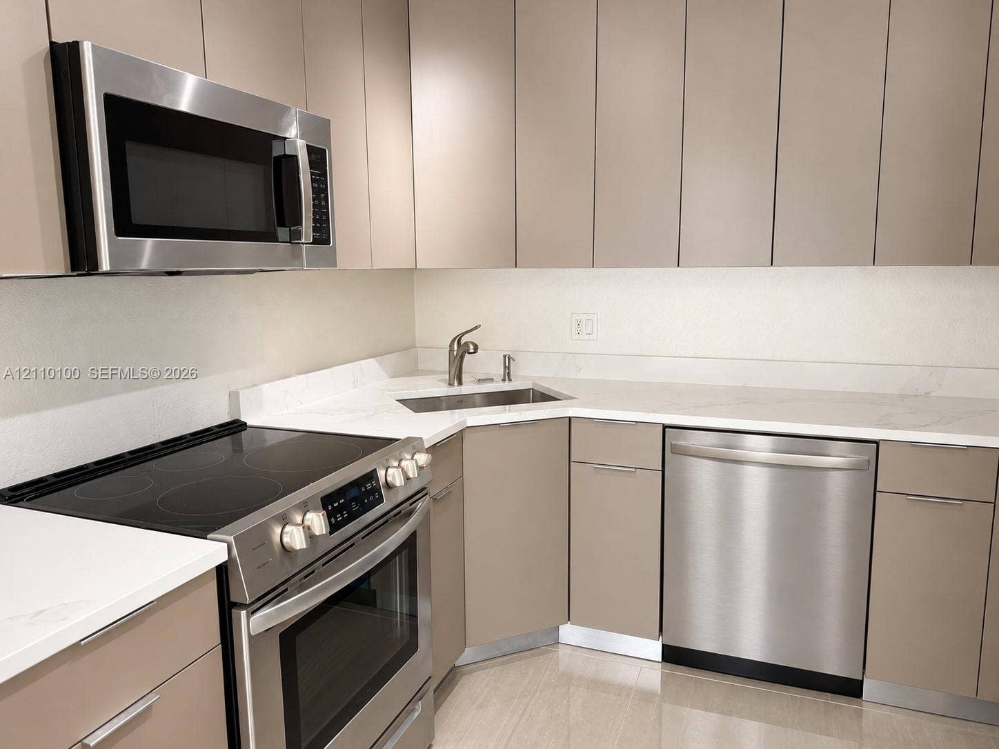 Kitchen featuring matte-finish flat-panel cabinetry, light-toned stone-style countertops, stainless steel appliances, a built-in microwave, and an undermount corner sink with a high-arch faucet