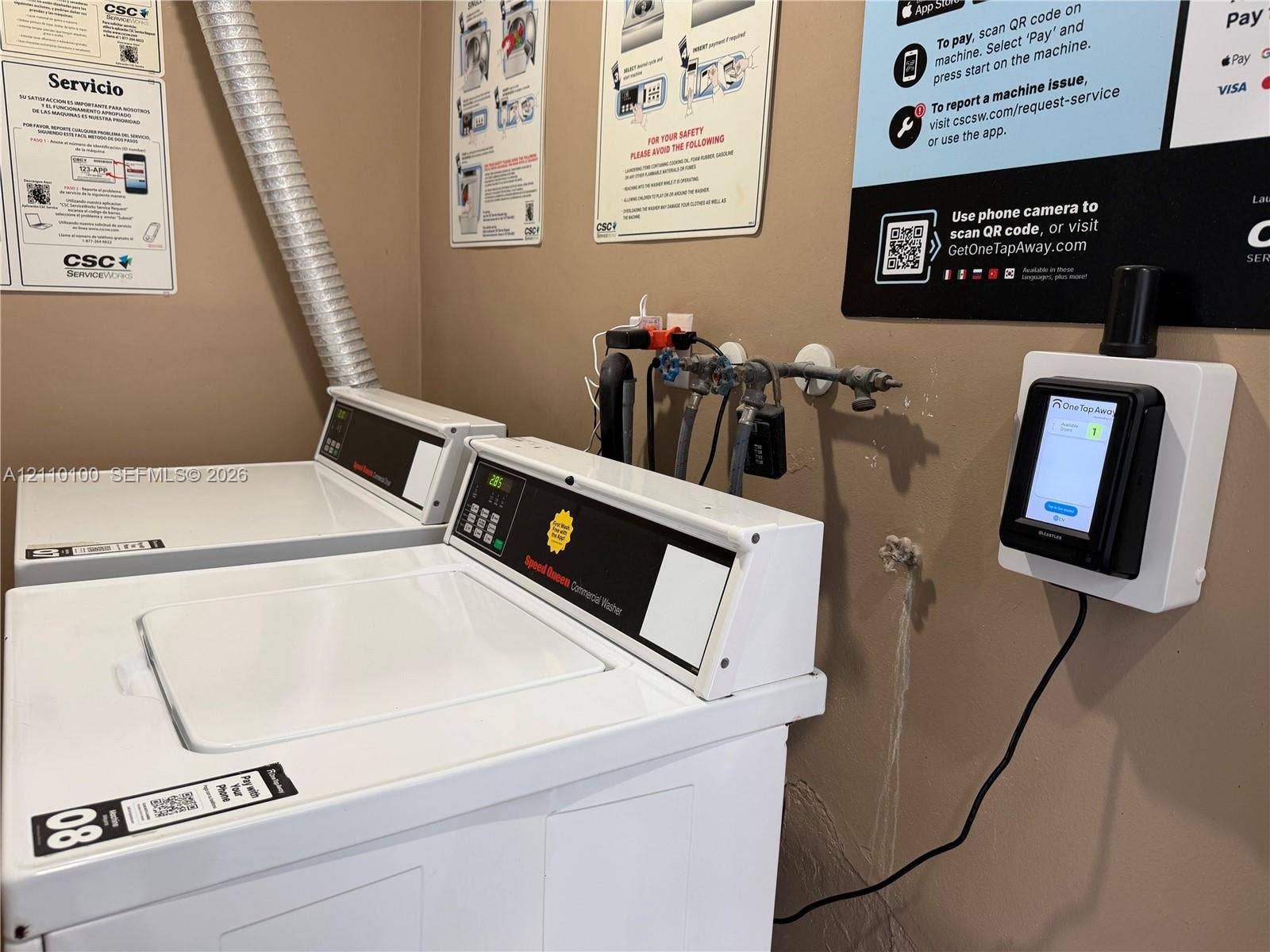 Commercial-grade top-load washing machines featuring digital payment terminals and integrated wall-mounted service interfaces