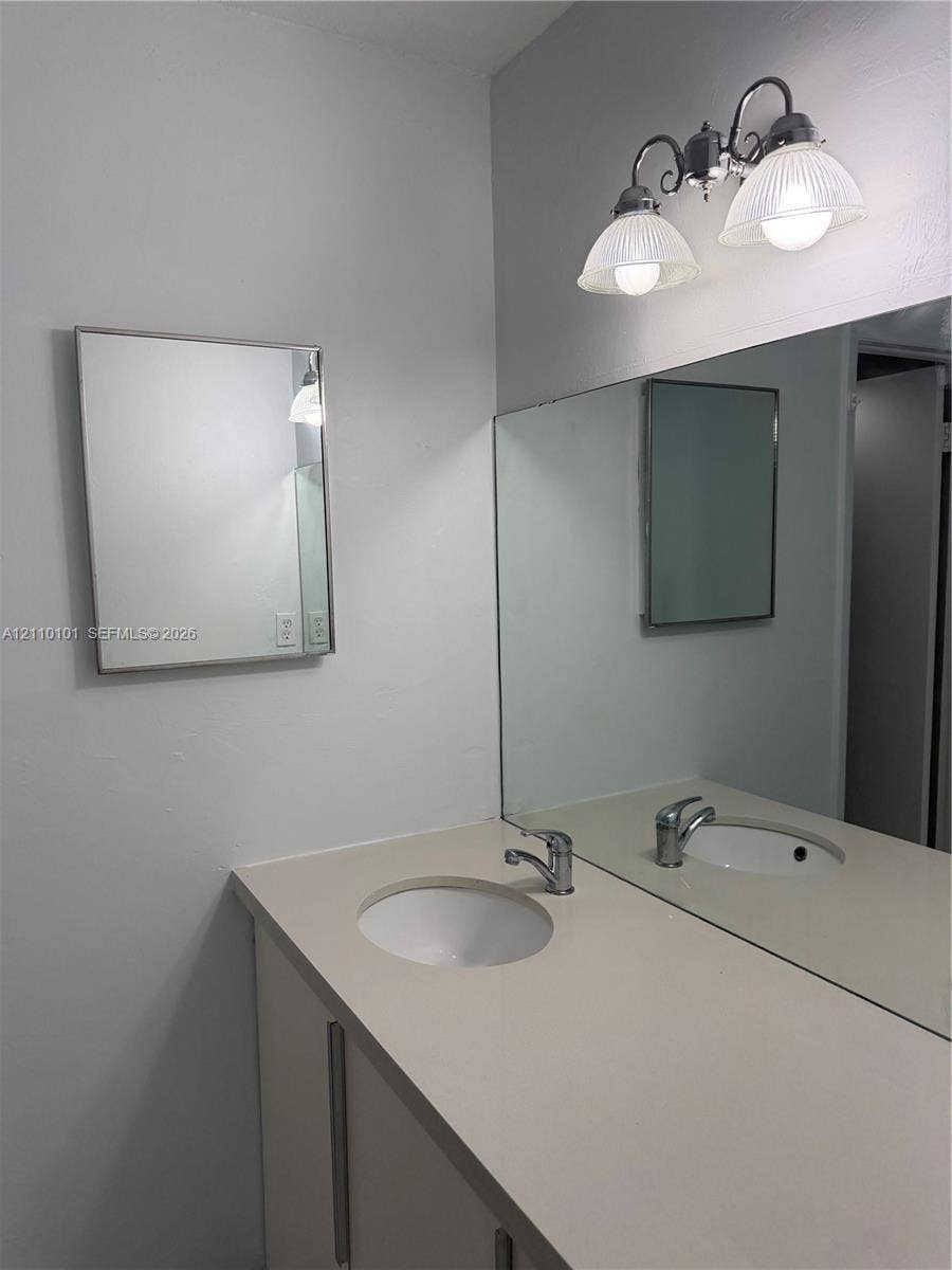 10850 N Kendall Drive, #412, Miami, Miami, FL 33176 Vanity featuring a solid-surface countertop, integrated basin, polished metal faucet, large wall-mounted mirror, and decorative dual-light fixture