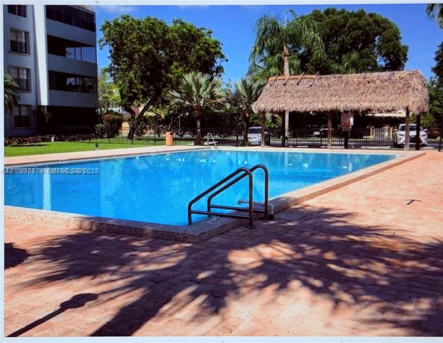 10850 N Kendall Drive, #412, Miami, Miami, FL 33176 Swimming pool featuring a paved deck, metal handrail, and a thatched-roof cabana structure