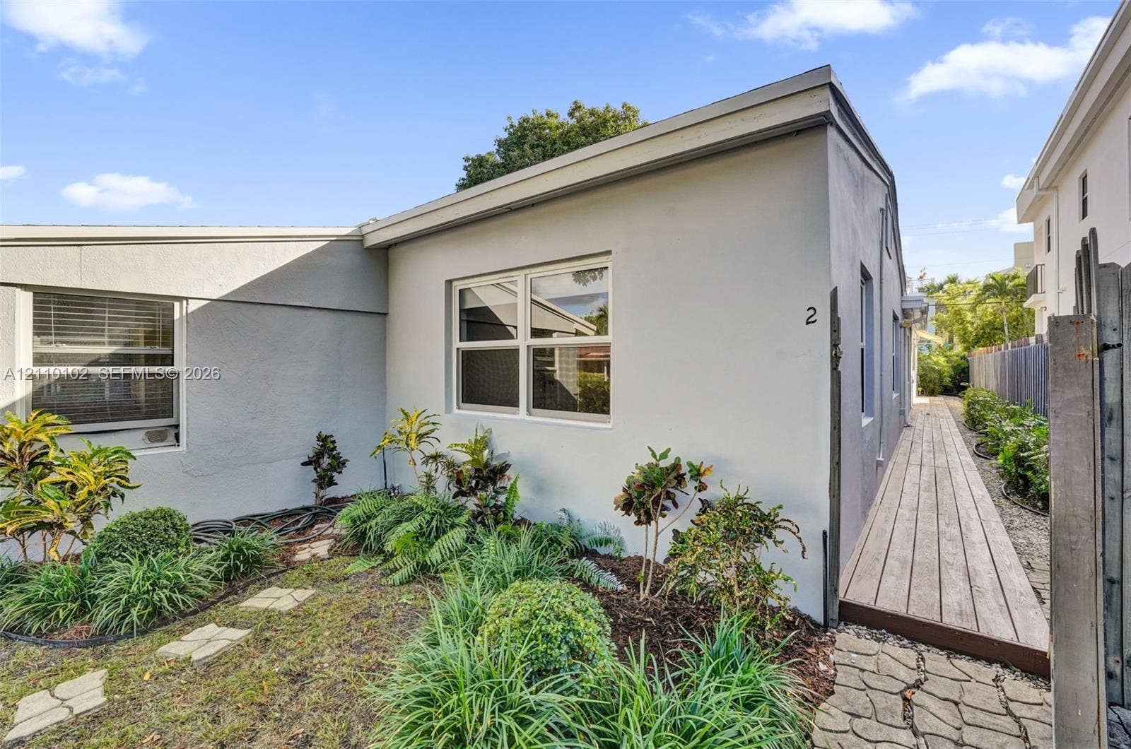 1224 NE 13th Avenue, #2, Fort Lauderdale, Fort Lauderdale, FL 33304 Smooth stucco exterior featuring dual-pane windows, a wooden boardwalk, and a stone-paver walkway bordered by ornamental landscaping
