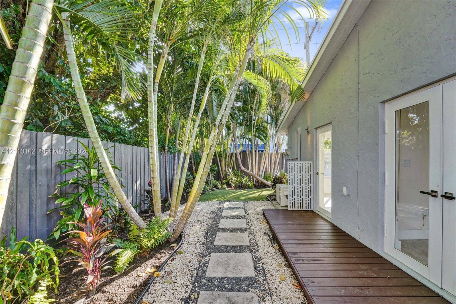 1224 NE 13th Avenue, #2, Fort Lauderdale, Fort Lauderdale, FL 33304 Exterior side yard featuring a wood-finish deck, a stone paver walkway, decorative gravel, vertical wood fencing, and mature palm trees