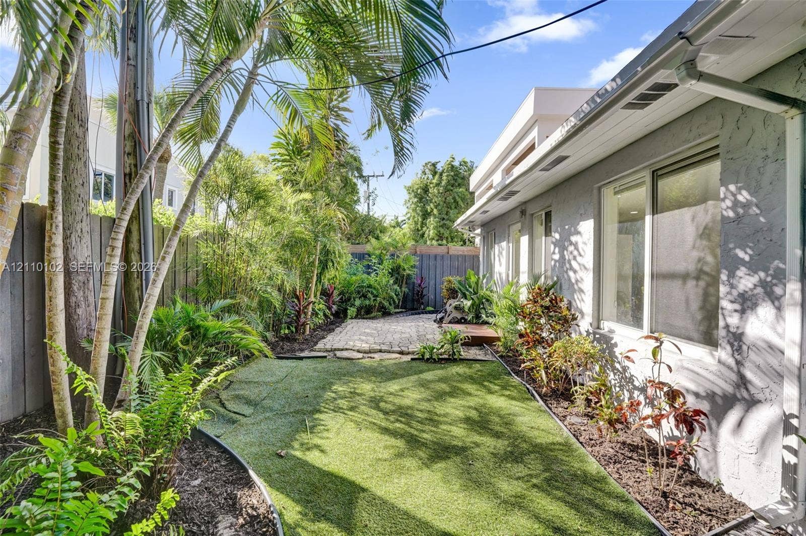 1224 NE 13th Avenue, #2, Fort Lauderdale, Fort Lauderdale, FL 33304 Side yard featuring artificial turf, stone paver accents, established tropical landscaping, and full-height wood fencing