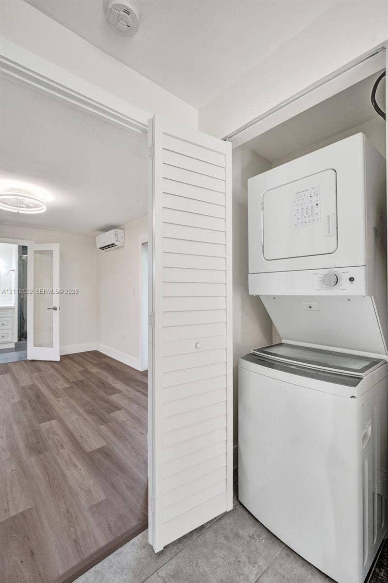 1224 NE 13th Avenue, #2, Fort Lauderdale, Fort Lauderdale, FL 33304 Stackable laundry unit featuring a top-load washer and front-load dryer set behind white louvered closet doors, complemented by wood-finish flooring and a wall-mounted ductless climate control system