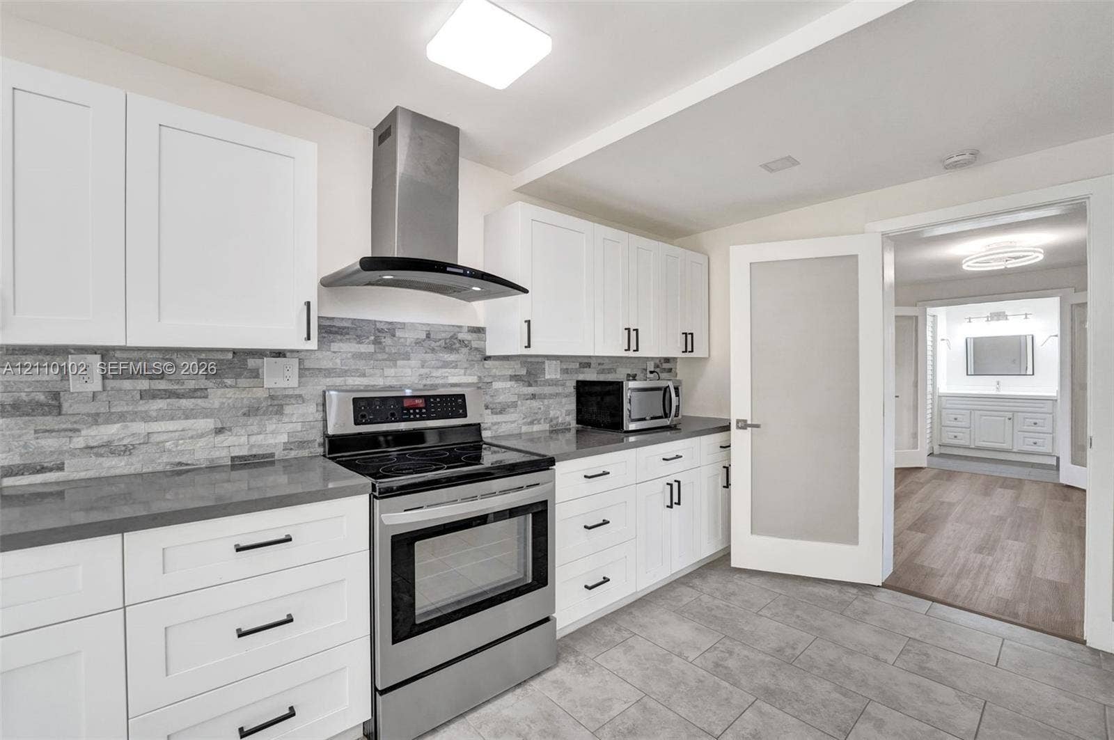 1224 NE 13th Avenue, #2, Fort Lauderdale, Fort Lauderdale, FL 33304 Kitchen featuring white shaker cabinetry, stainless steel appliances including a range and range hood, stone-finish backsplash, solid-surface countertops, and tiled flooring