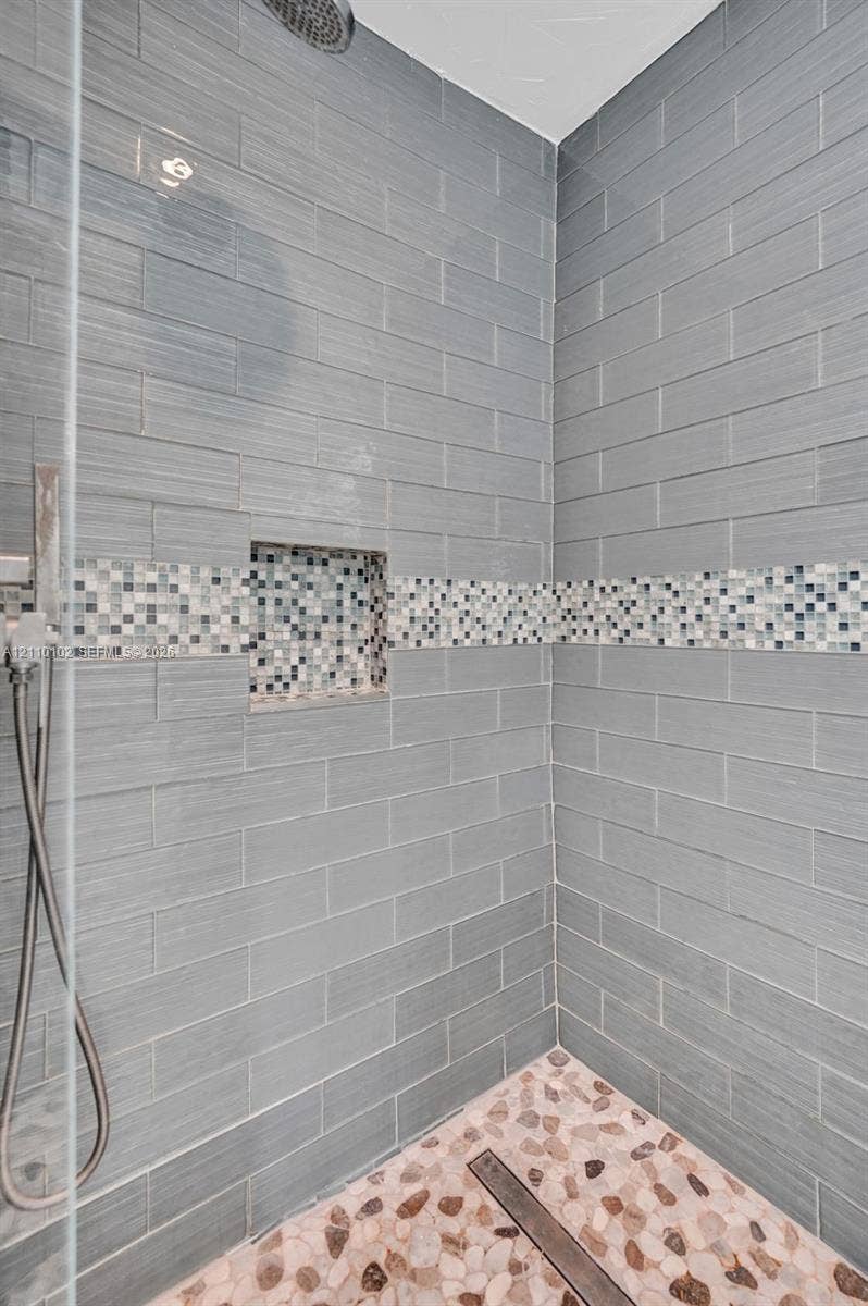1224 NE 13th Avenue, #2, Fort Lauderdale, Fort Lauderdale, FL 33304 Walk-in shower featuring grey subway-style wall tile, a decorative glass mosaic accent band, a built-in recessed wall niche, a pebble-stone floor, and a handheld shower fixture