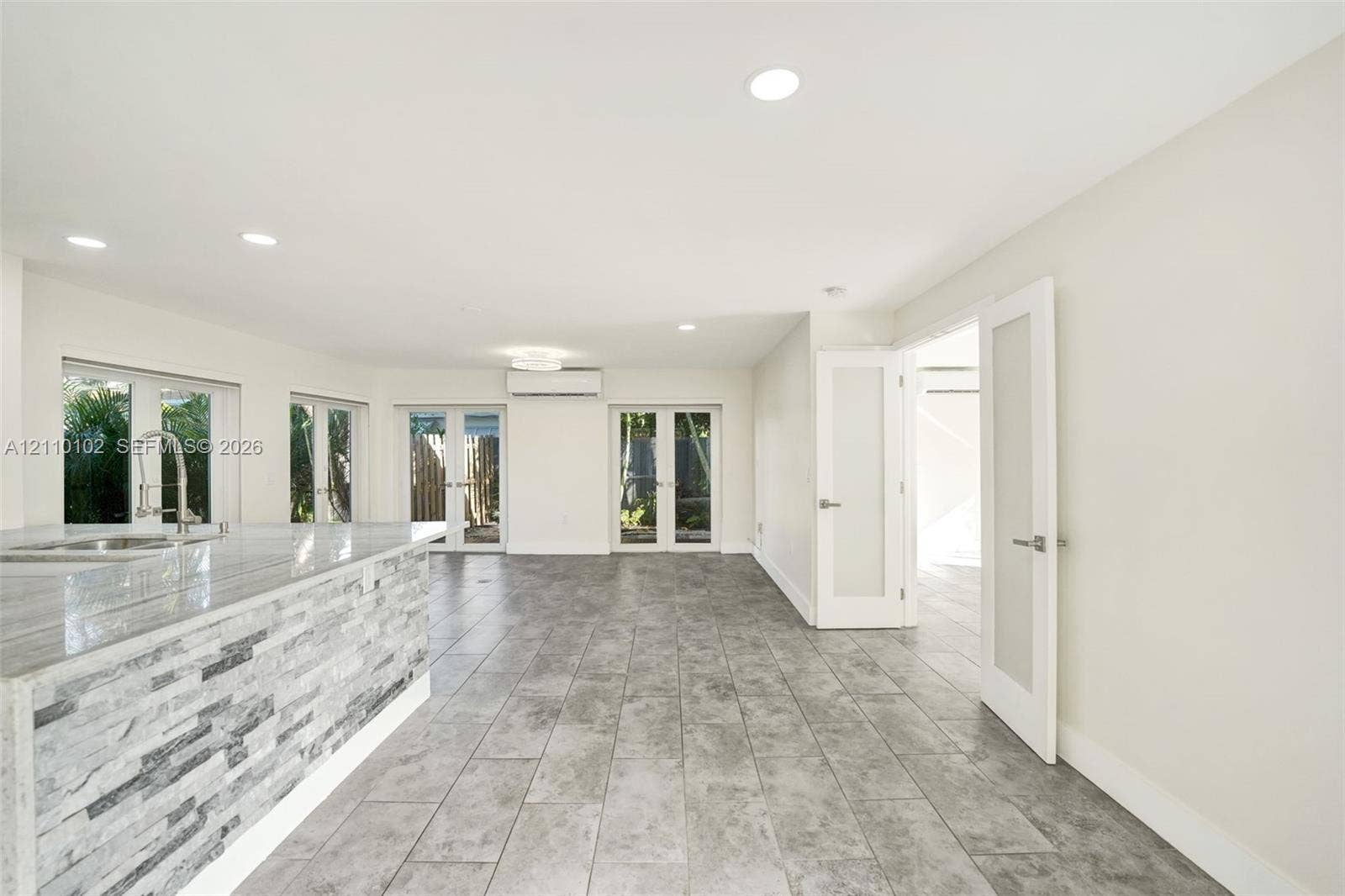 1224 NE 13th Avenue, #2, Fort Lauderdale, Fort Lauderdale, FL 33304 Open-concept interior featuring large-format tile flooring, stone-veneer kitchen island base, recessed lighting, wall-mounted climate control unit, and glass-paneled entry doors