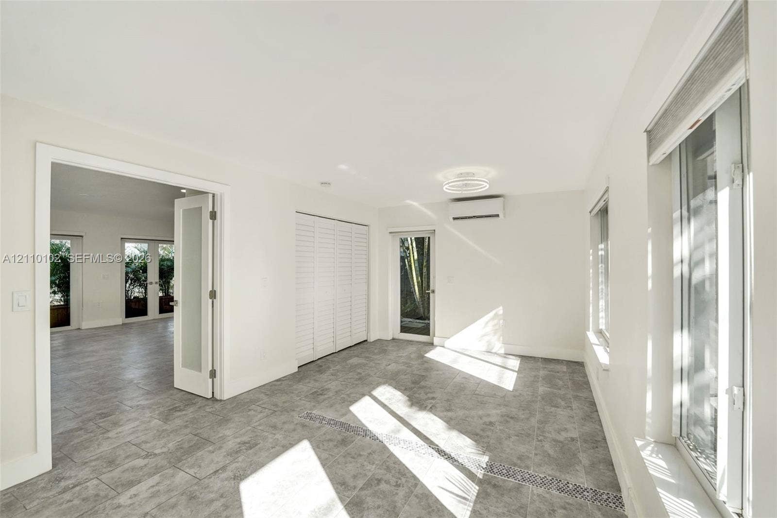 1224 NE 13th Avenue, #2, Fort Lauderdale, Fort Lauderdale, FL 33304 Interior space featuring large-format tile flooring, double glass-paneled doors, built-in closet cabinetry with louvered doors, wall-mounted air conditioning unit, and flush-mount LED circular ceiling light