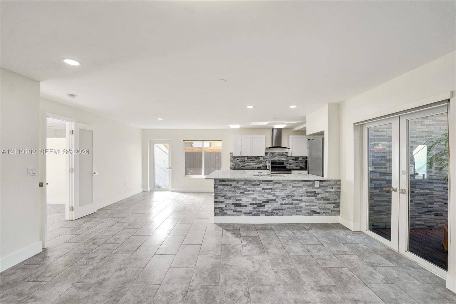 1224 NE 13th Avenue, #2, Fort Lauderdale, Fort Lauderdale, FL 33304 Open-concept interior featuring large-format ceramic tile flooring, kitchen island with stone-finish cladding, quartz countertops, stainless steel appliances, and French doors