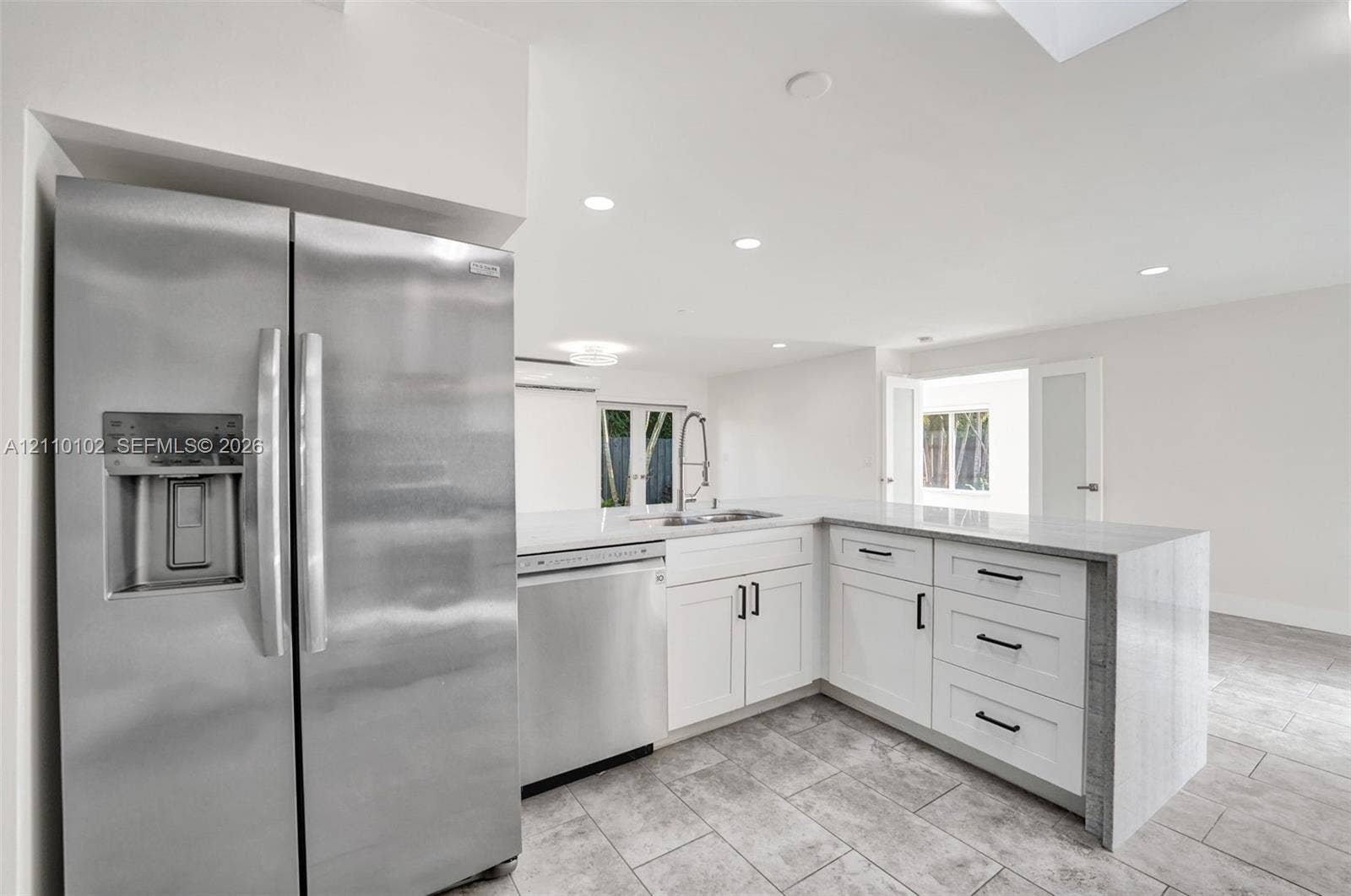 1224 NE 13th Avenue, #2, Fort Lauderdale, Fort Lauderdale, FL 33304 Kitchen featuring white shaker-style cabinetry, stainless steel appliances, quartz countertops, a waterfall-edge peninsula, and stone-tile flooring