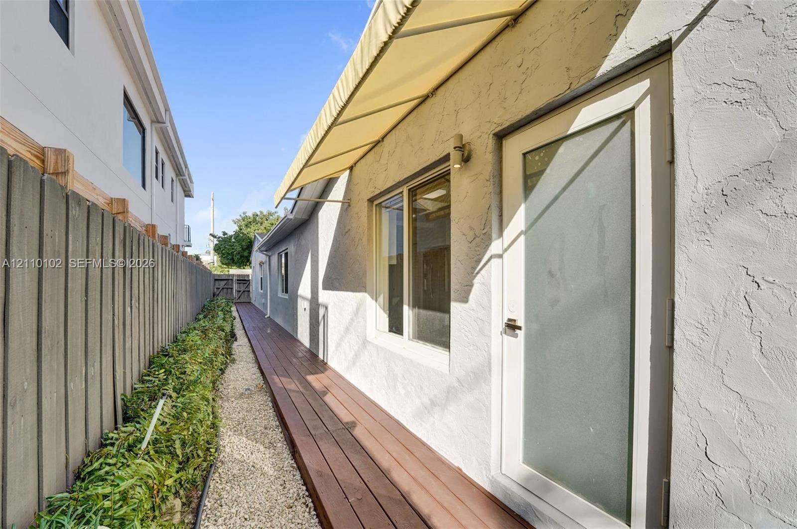 1224 NE 13th Avenue, #2, Fort Lauderdale, Fort Lauderdale, FL 33304 Stucco exterior featuring a wood-finish deck, retractable fabric awning, frosted-glass entry door, and perimeter privacy fencing