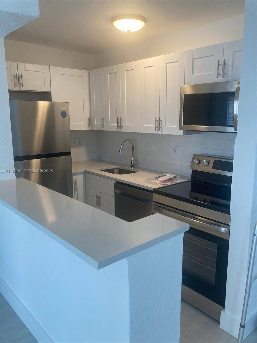 Kitchen featuring white shaker-style cabinetry, quartz countertops, stainless steel appliances, and a peninsula with breakfast bar seating