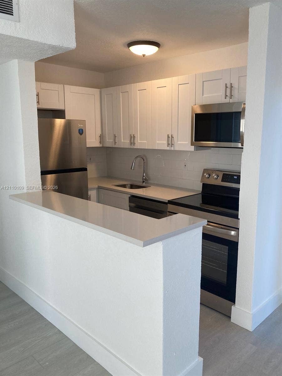 Kitchen featuring white cabinetry, quartz countertops, stainless steel appliances, a subway tile backsplash, and a breakfast bar