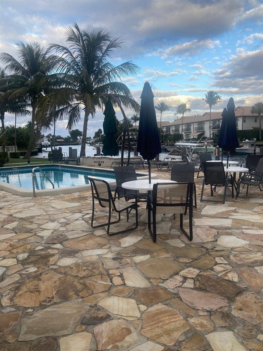Flagstone patio featuring an in-ground pool, waterfront bulkhead, and mature palm trees