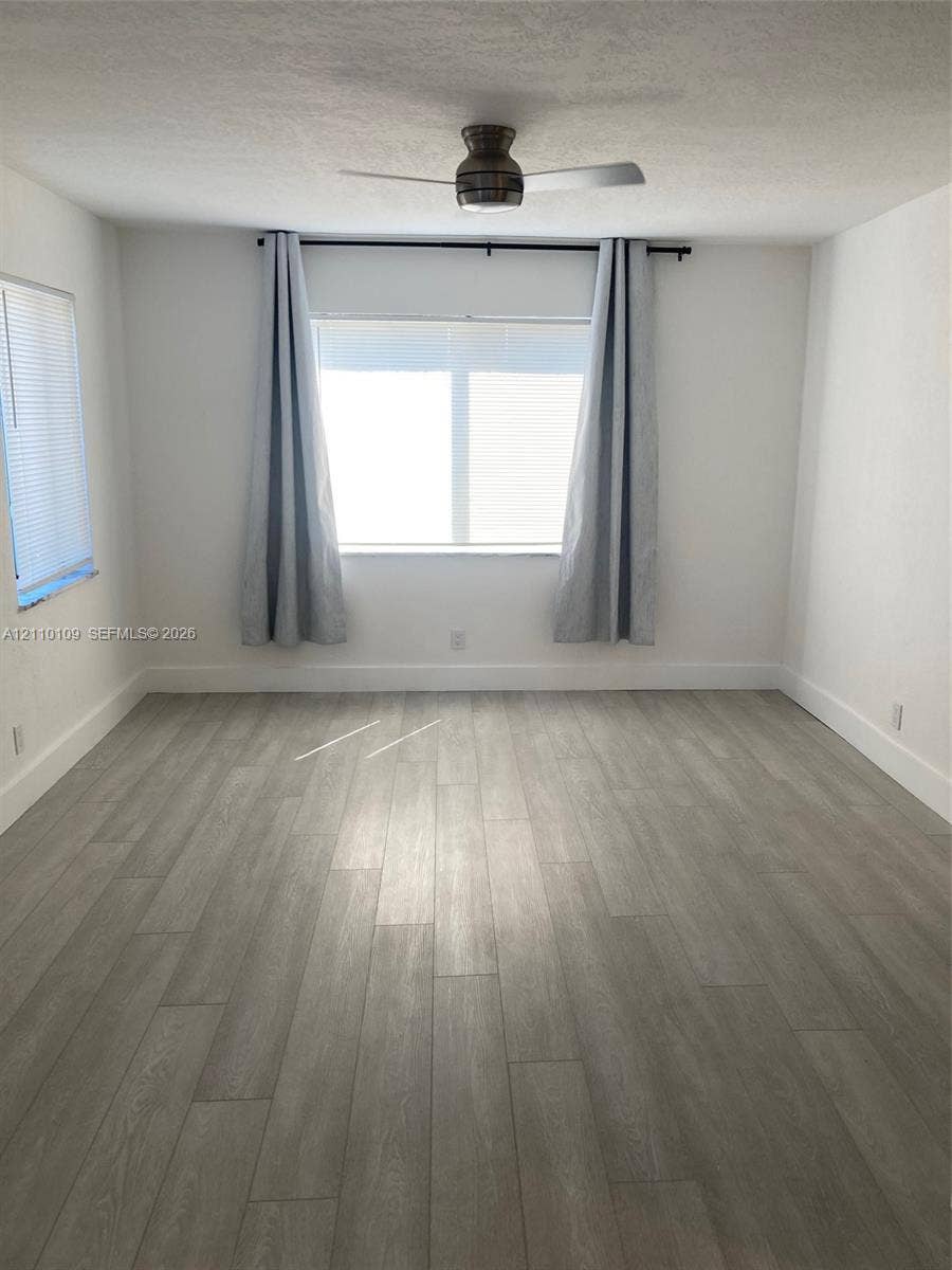 Neutral-toned interior space featuring wood-finish flooring, dual windows, and a ceiling-mounted fan