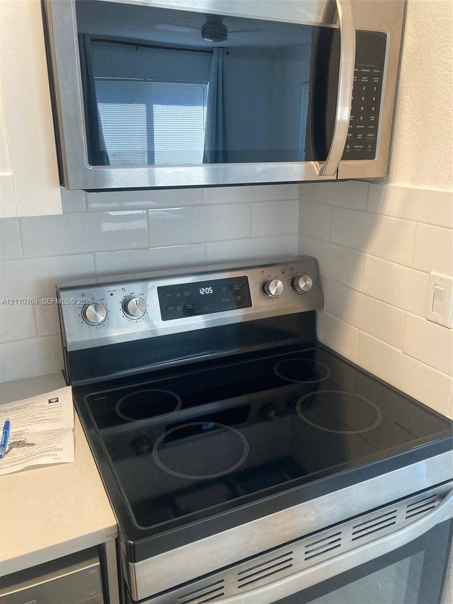 Stainless steel electric range and built-in microwave, white subway tile backsplash, and solid surface countertop