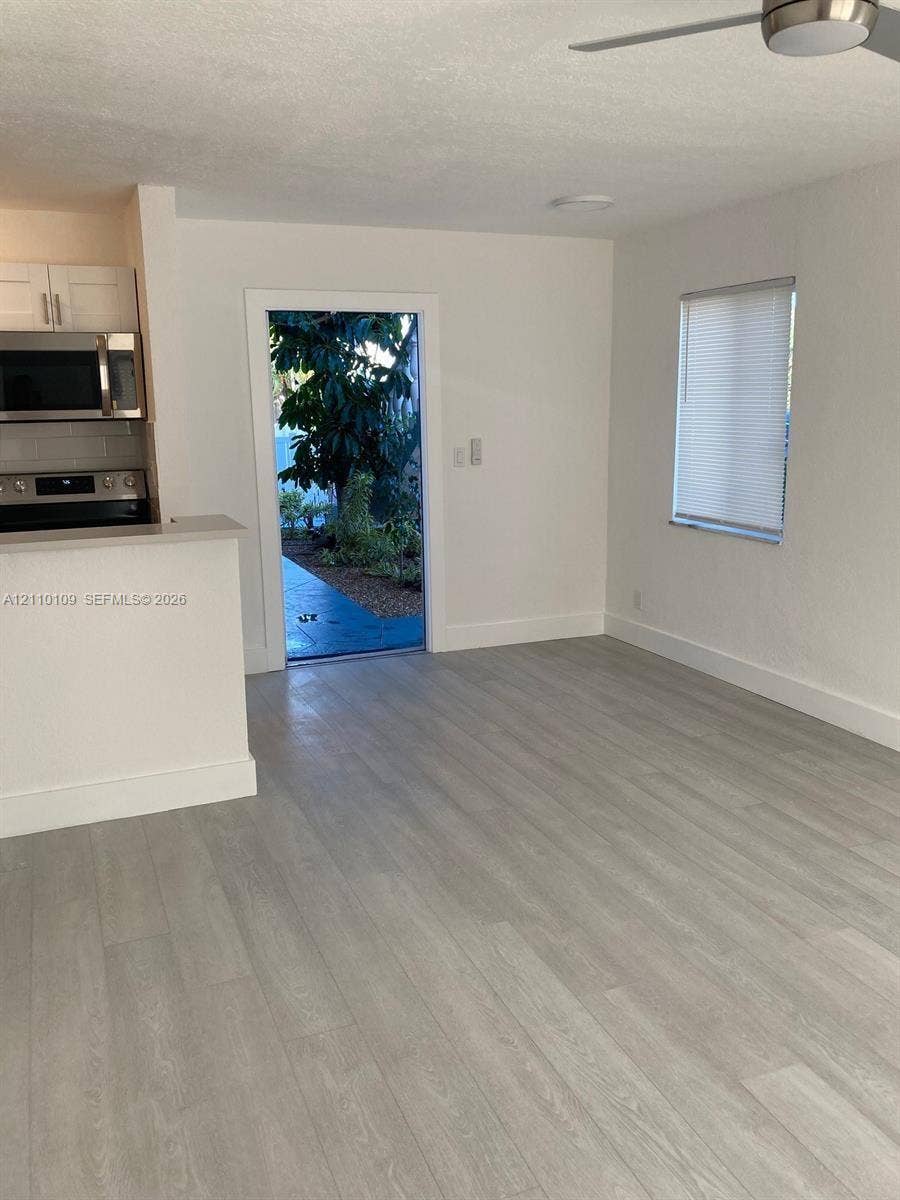 Open-concept interior featuring light wood-finish flooring, white cabinetry, stainless steel appliances, and a ceiling fan