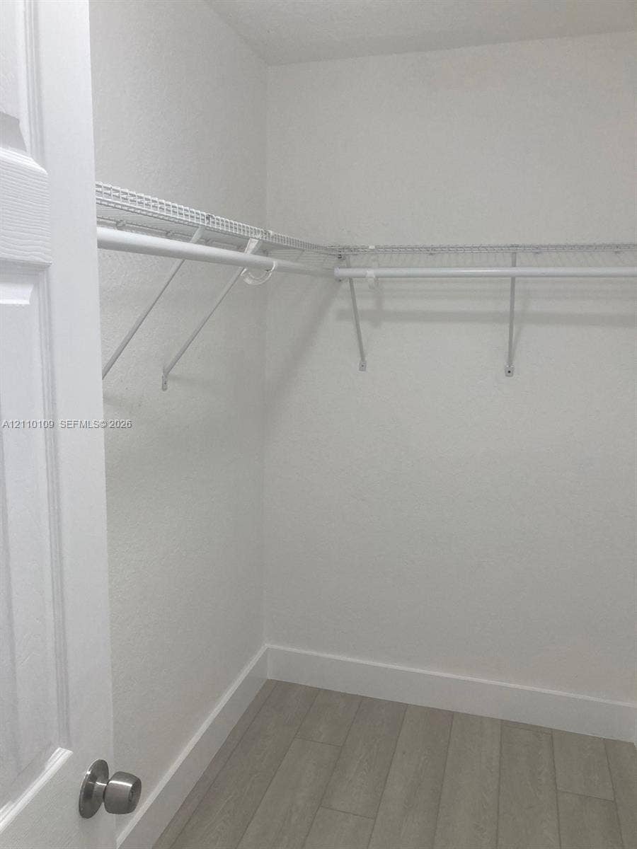 Storage area featuring neutral wood-finish flooring and white wire shelving with integrated hanging rods