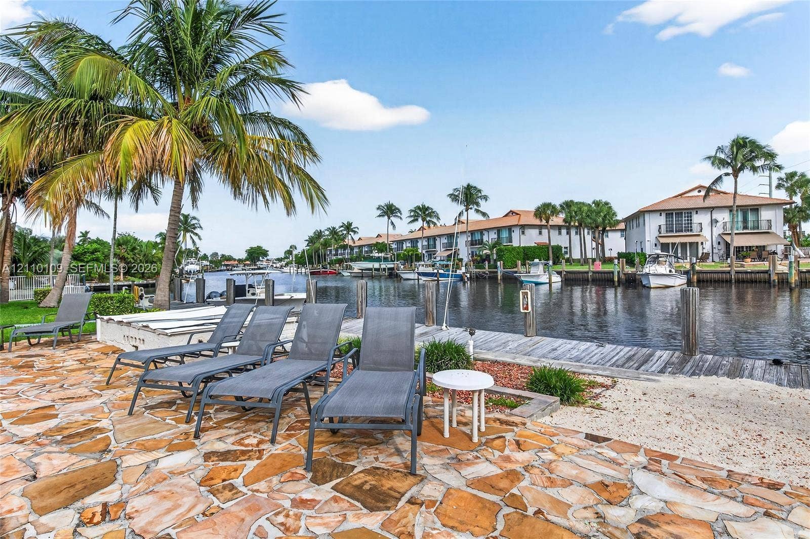 Waterfront property featuring a stone paver patio, wooden bulkhead dock, and mature palm trees