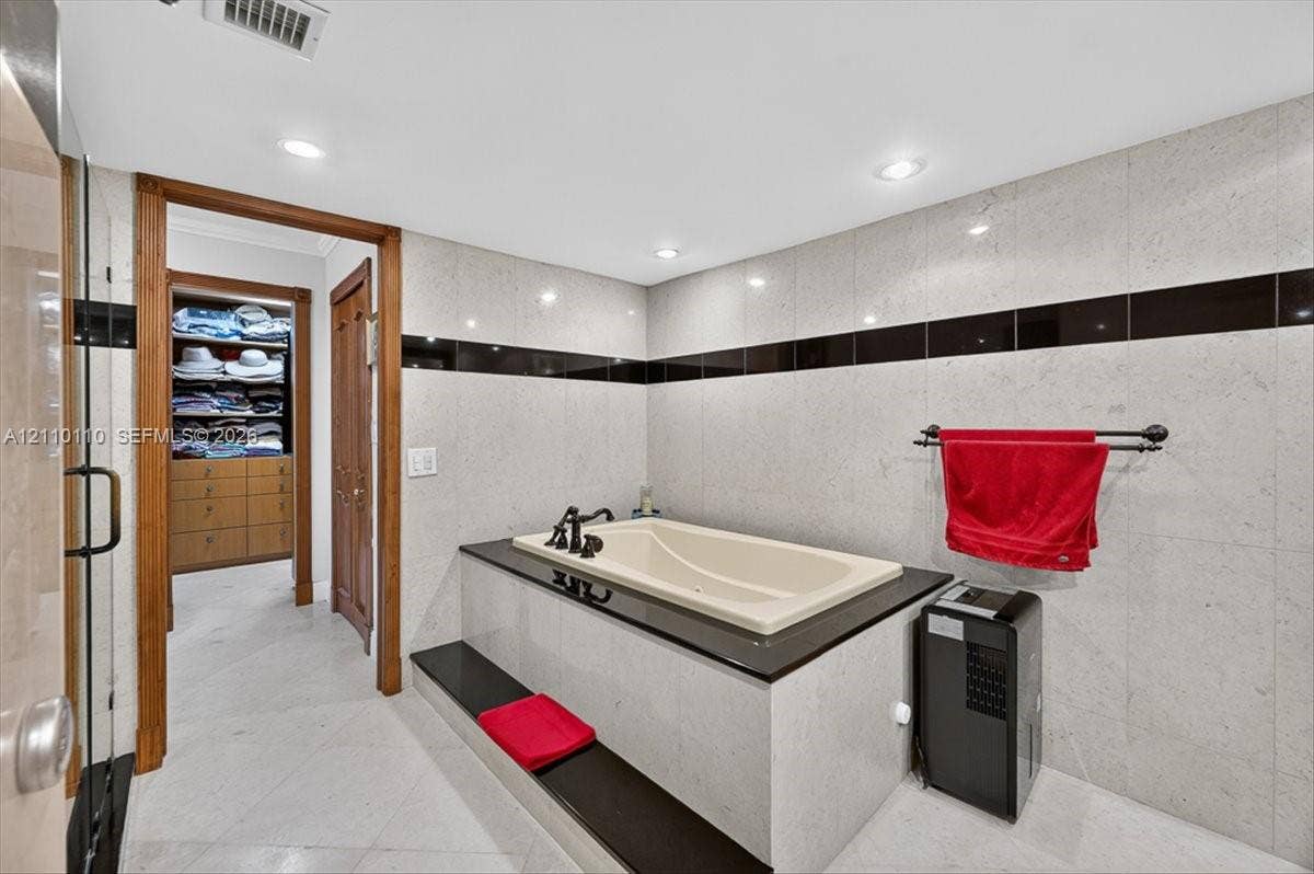 2751 S Ocean Drive, #801N, Hollywood, FL 33019 Soaking tub featuring a black stone surround and deck, recessed lighting, floor-to-ceiling wall tile with black accent inlay, and wood-finish built-in closet cabinetry