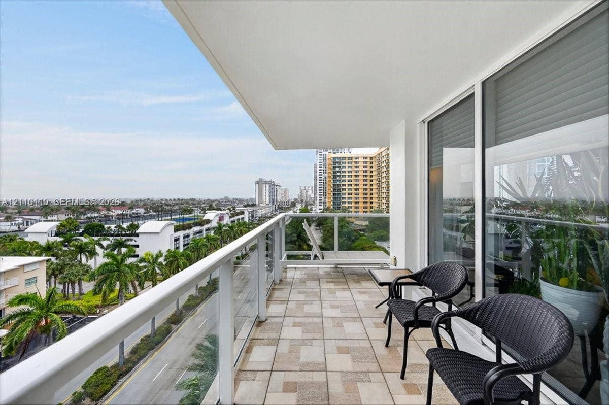 2751 S Ocean Drive, #801N, Hollywood, FL 33019 Covered balcony featuring geometric tile flooring, a white metal and glass panel railing, and expansive floor-to-ceiling sliding glass doors