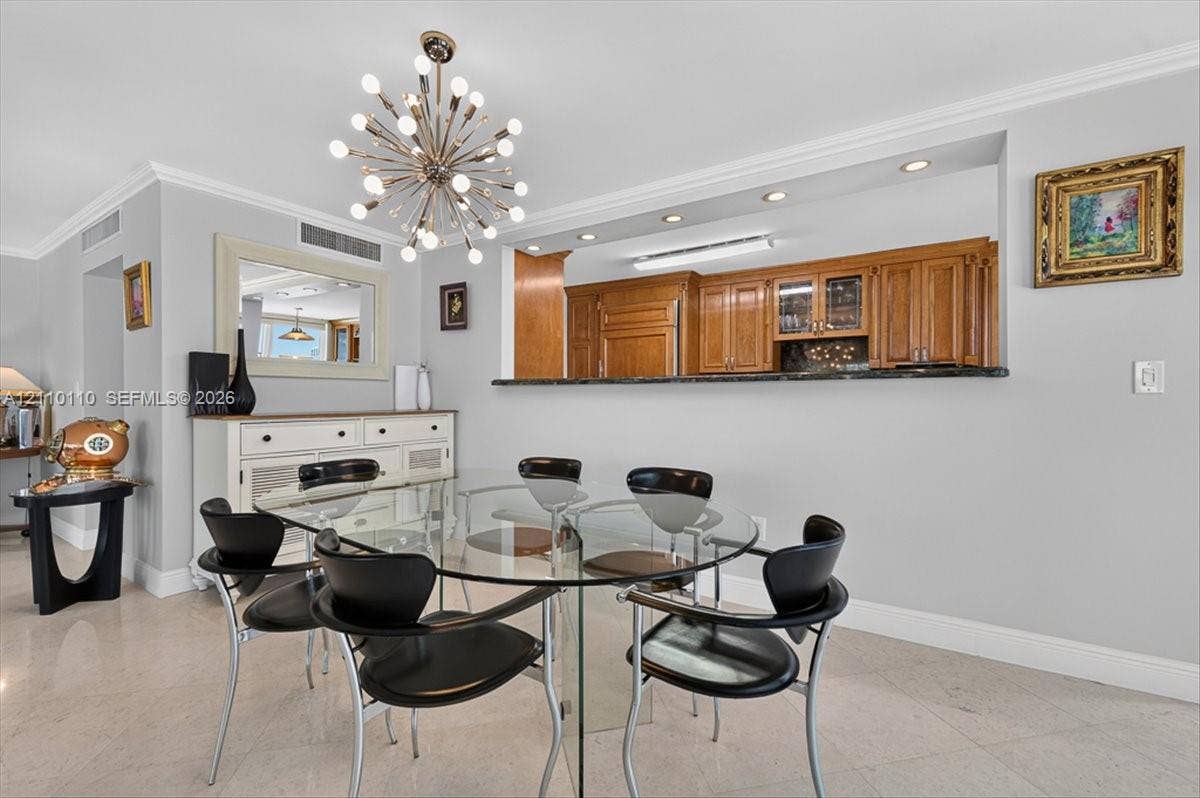 2751 S Ocean Drive, #801N, Hollywood, FL 33019 Dining area featuring stone flooring, a decorative multi-bulb pendant fixture, crown molding, and a pass-through opening with a stone countertop