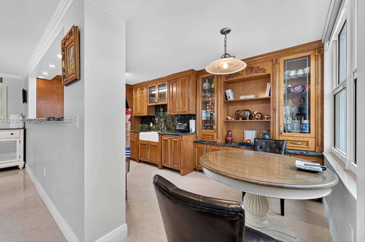 2751 S Ocean Drive, #801N, Hollywood, FL 33019 Custom wood cabinetry featuring integrated display shelving and glass-front upper units, apron-front farmhouse sink, stone countertops, and crown molding