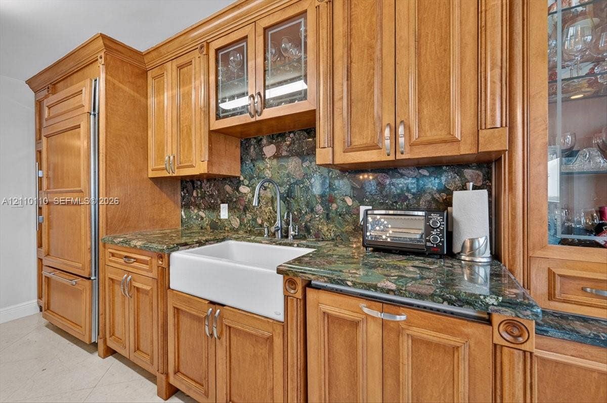 2751 S Ocean Drive, #801N, Hollywood, FL 33019 Kitchen featuring custom wood cabinetry, integrated refrigerator, stone countertops, full-height decorative stone backsplash, and a white farmhouse-style sink