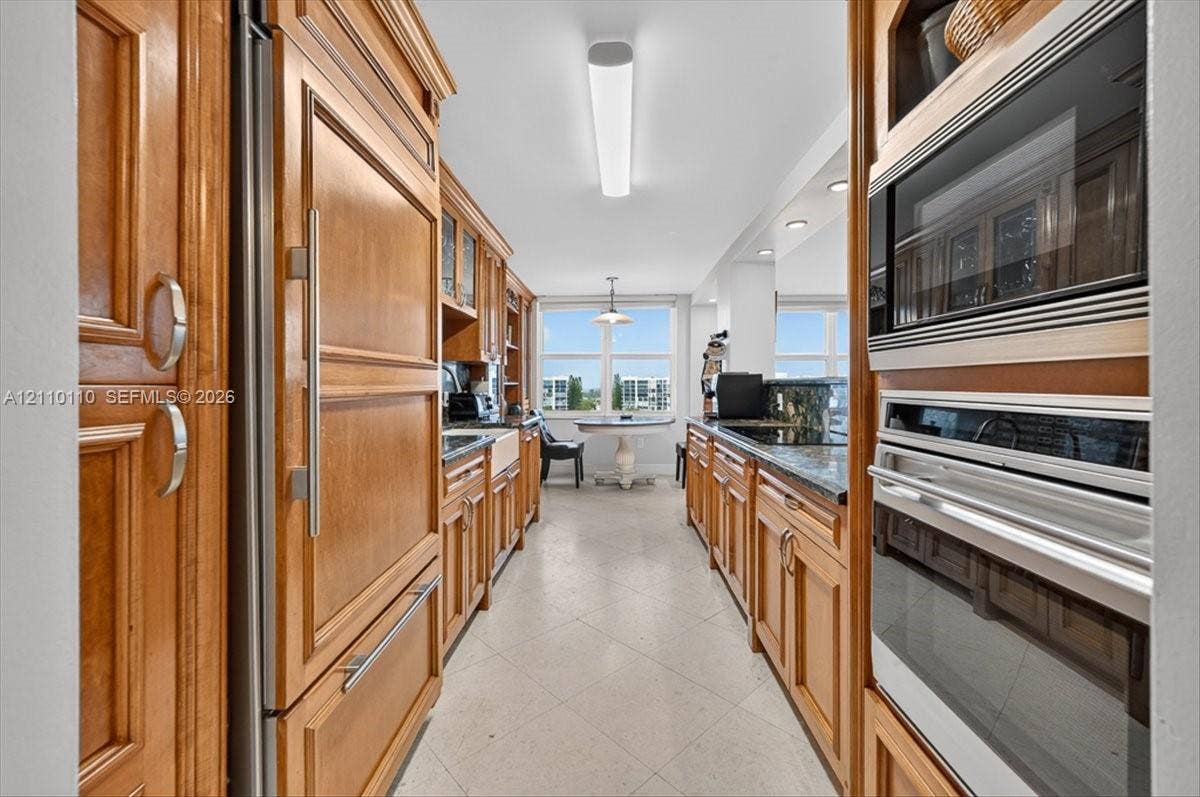 2751 S Ocean Drive, #801N, Hollywood, FL 33019 Kitchen featuring natural wood cabinetry, built-in panel-ready refrigerator, stainless steel double wall oven and microwave, dark stone countertops, and tile flooring
