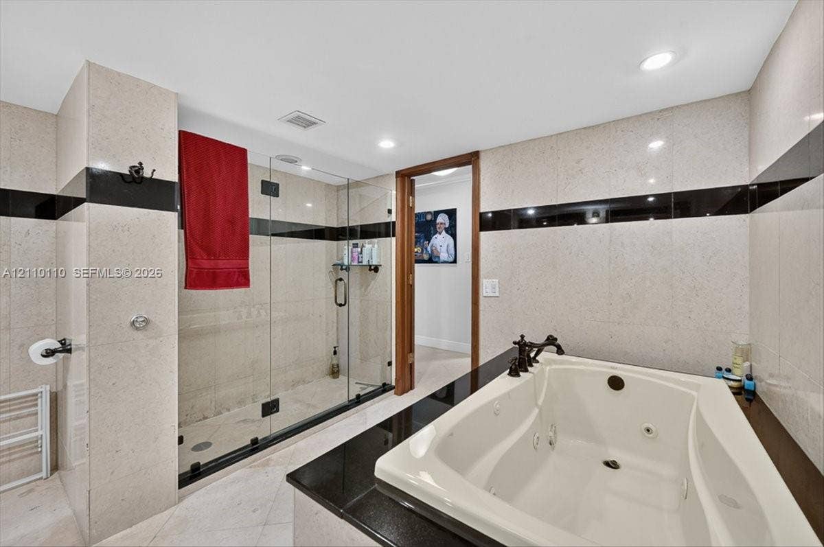 2751 S Ocean Drive, #801N, Hollywood, FL 33019 Bathroom featuring a jetted soaking tub with a black stone surround, a glass-enclosed walk-in shower, wall-to-wall light-toned tile with black inlay accents, and recessed lighting