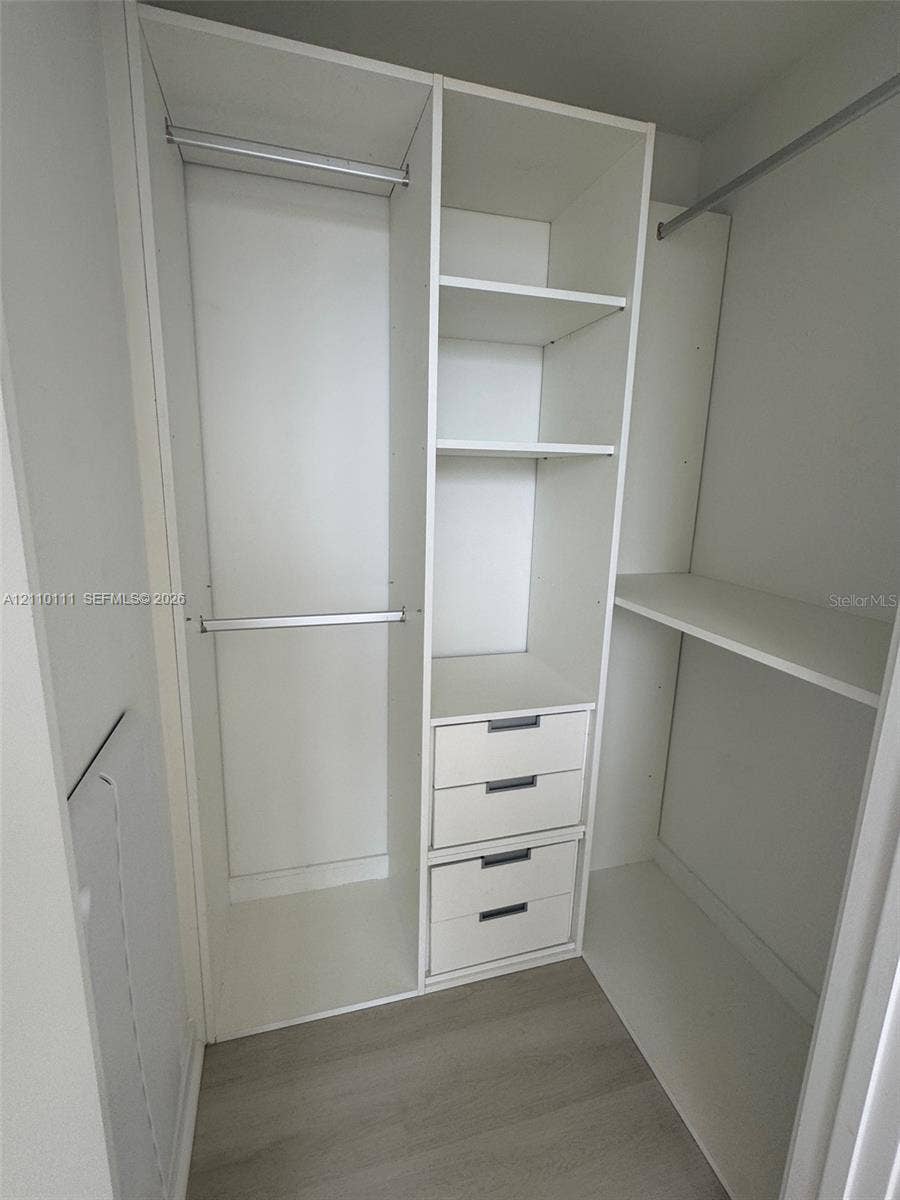 5563 Millenia Park Boulevard, #315, Orlando, Orlando, FL 32839 Custom walk-in closet featuring white built-in shelving, a central tower of three drawers, dual hanging rods, and wood-finish flooring