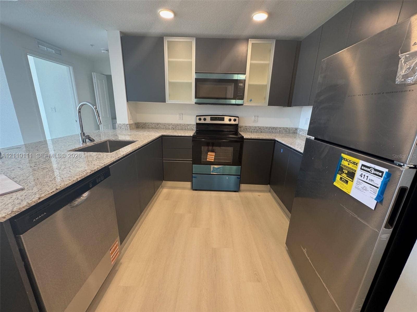 5563 Millenia Park Boulevard, #315, Orlando, Orlando, FL 32839 Kitchen featuring flat-panel cabinetry, light-toned stone-finish countertops, stainless steel appliances, a stainless steel undermount sink with a high-arch faucet, and light wood-finish flooring
