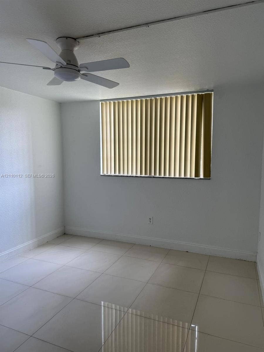 14185 SW 87th Street, #A110, Miami, FL 33183 Neutral-toned tile flooring, white-painted walls, ceiling-mounted fan, and vertical window blinds
