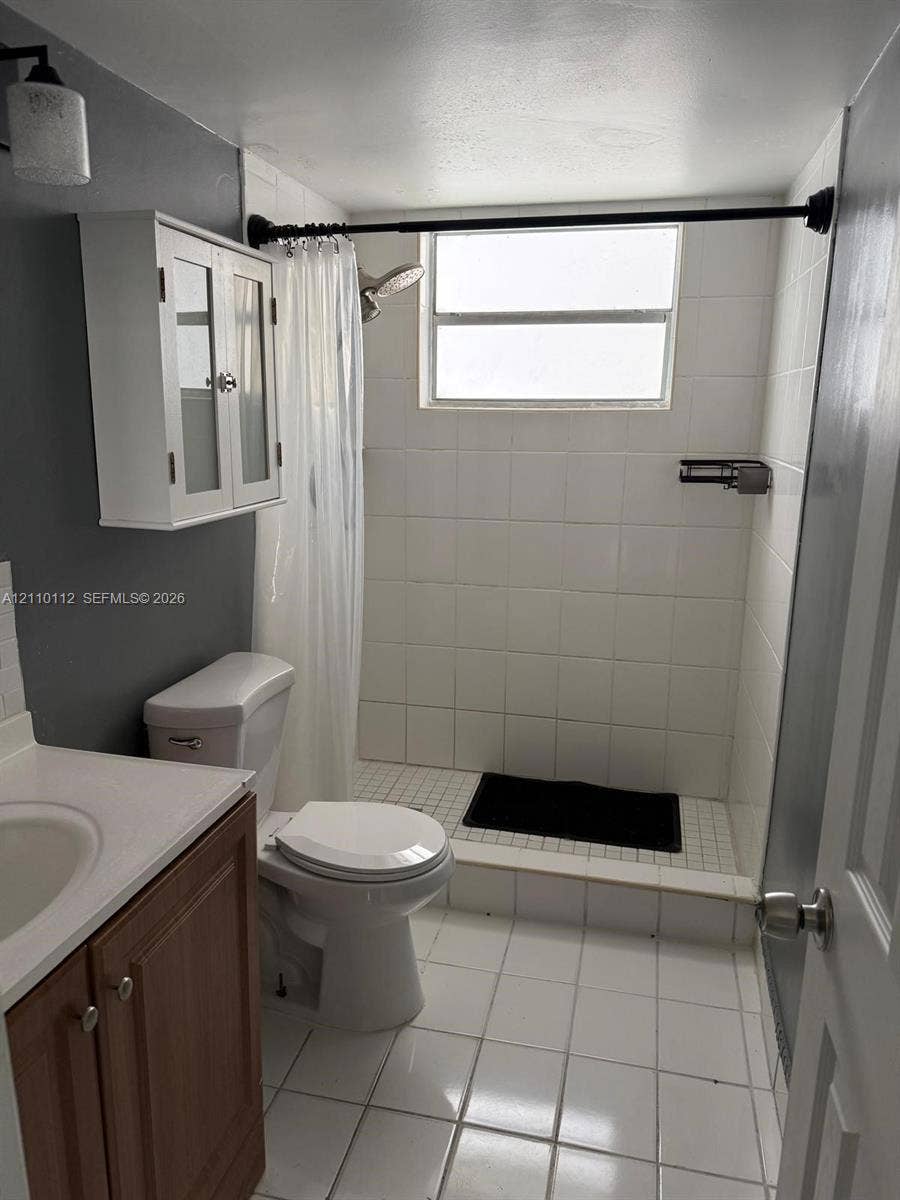 14185 SW 87th Street, #A110, Miami, FL 33183 Bathroom featuring white tile flooring, a shower with white wall tile, a wood-finish vanity with a sink, and a white wall-mounted storage cabinet