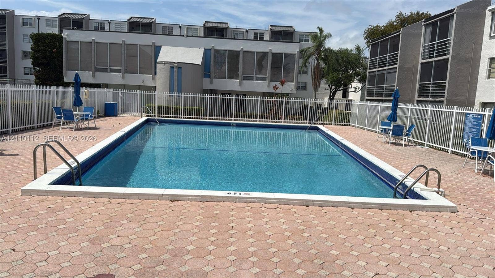 14185 SW 87th Street, #A110, Miami, FL 33183 Rectangular swimming pool featuring metal access ladders and a concrete paver deck enclosed by a white fence