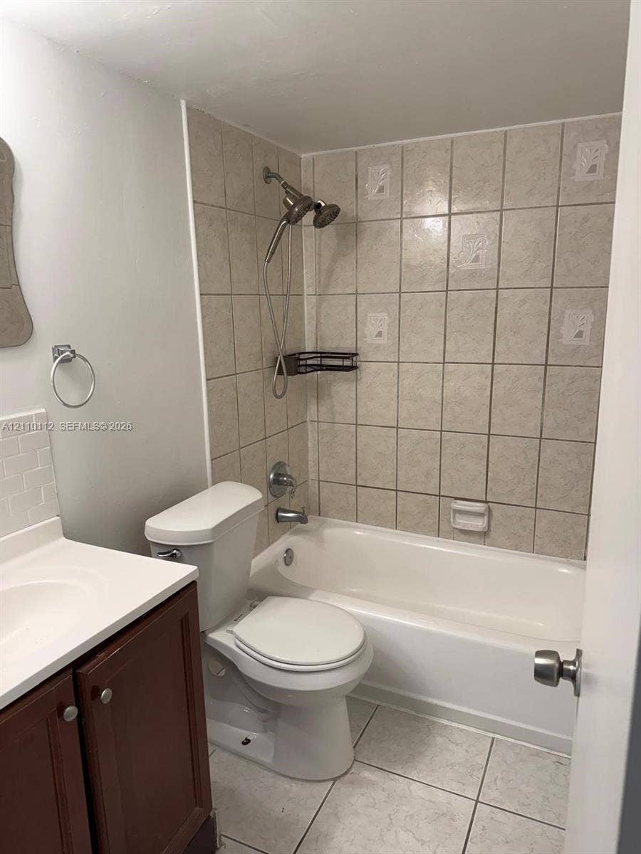 14185 SW 87th Street, #A110, Miami, FL 33183 Bathroom featuring a wood-finish vanity with a white countertop, a white porcelain toilet, and a bathtub with a tiled surround and an adjustable handheld showerhead