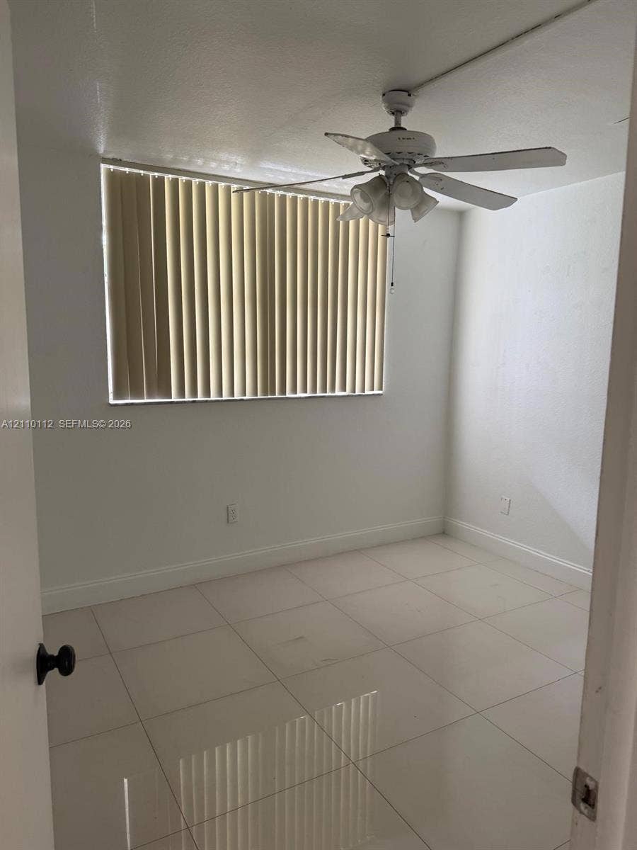 14185 SW 87th Street, #A110, Miami, FL 33183 Neutral interior space featuring large-format tile flooring, white wall finishes, a ceiling-mounted light fixture with fan, and vertical window blinds