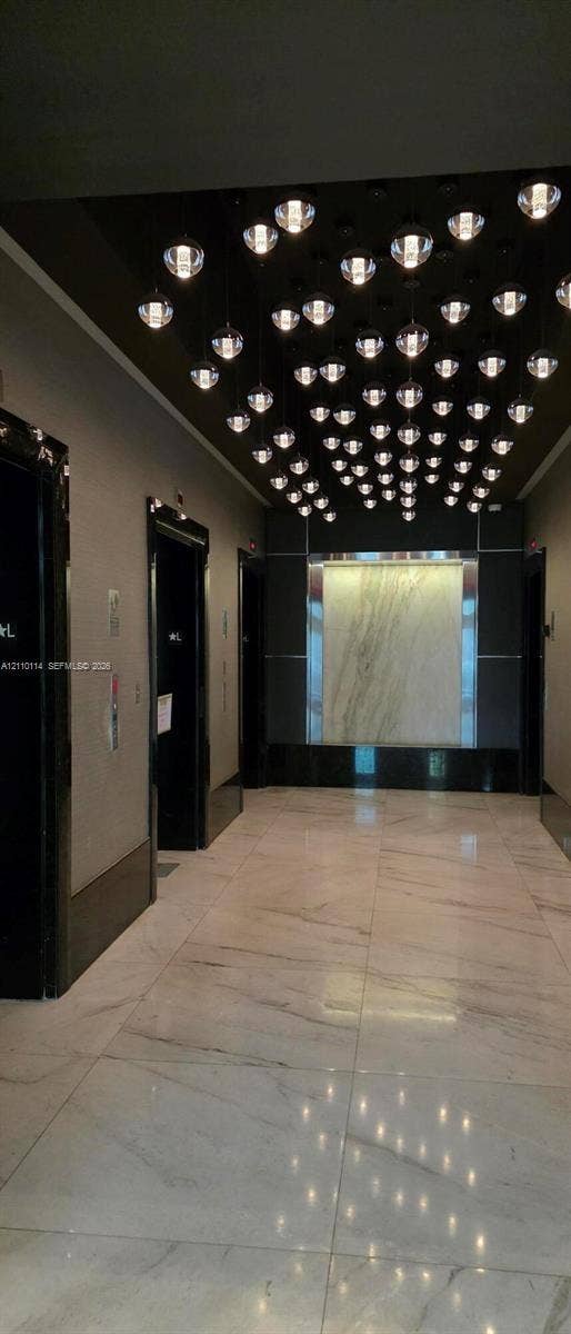 950 Brickell Bay Drive, #5108, Miami, Miami, FL 33131 Grand lobby featuring large-format polished stone flooring, custom multi-pendant ceiling lighting, stone wall accent paneling, and high-gloss door frames