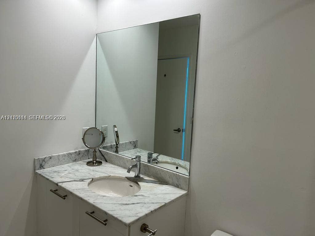 950 Brickell Bay Drive, #5108, Miami, Miami, FL 33131 Vanity featuring a stone-top counter, undermount sink, metal faucet, and built-in cabinetry with metal pulls, complemented by a large, wall-mounted mirror