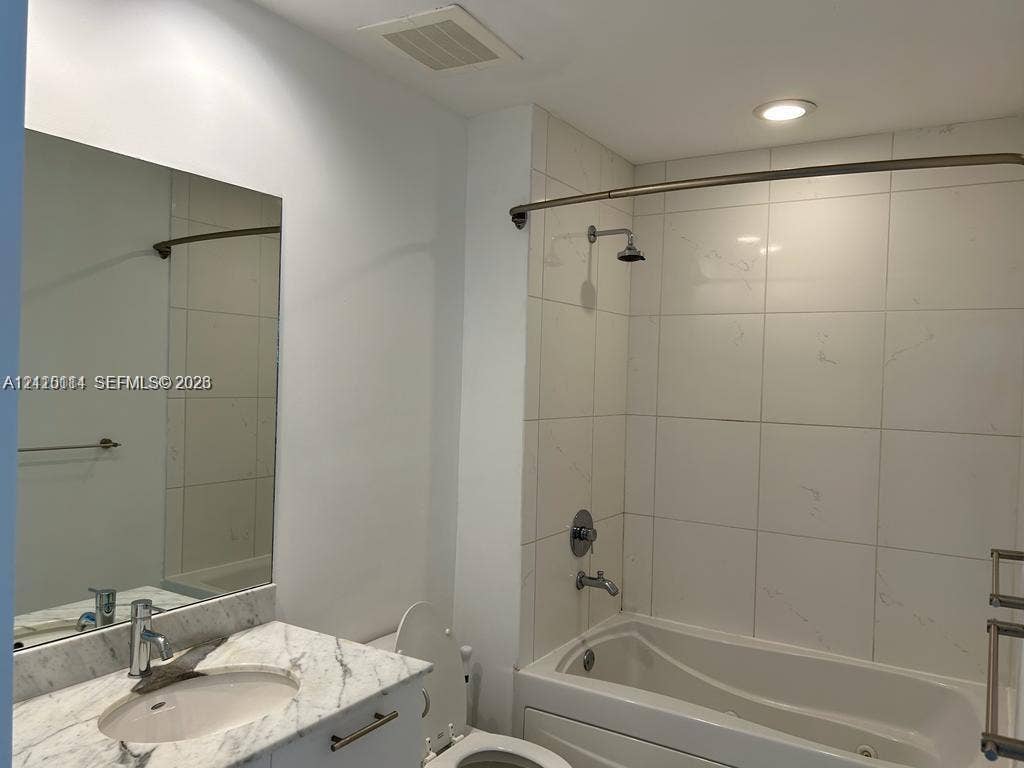 950 Brickell Bay Drive, #5108, Miami, Miami, FL 33131 Bathroom featuring a vanity with a light-toned stone countertop, integrated sink, wall-mounted mirror, tub-shower combination with full-height tile surround, and metallic hardware