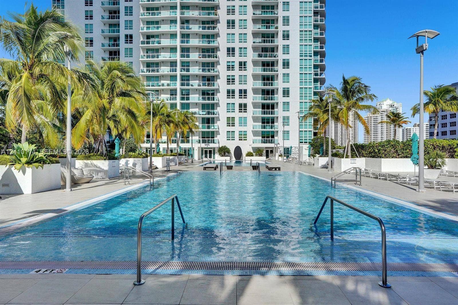 950 Brickell Bay Drive, #5108, Miami, Miami, FL 33131 Rectangular swimming pool with integrated entry steps and stainless steel handrails, surrounded by a paved deck, large white planters, and mature palm trees