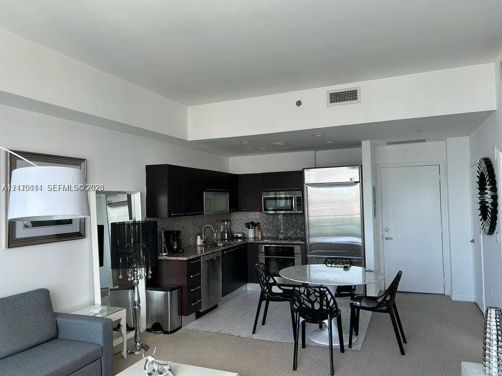 950 Brickell Bay Drive, #5108, Miami, Miami, FL 33131 Kitchen featuring dark-finish cabinetry, stainless steel appliances, stone-finish countertops, and tile flooring