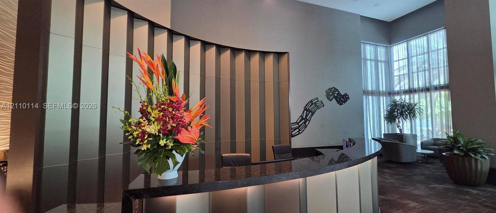 950 Brickell Bay Drive, #5108, Miami, Miami, FL 33131 Double-height lobby featuring a curved reception desk with a stone countertop, vertical metallic wall paneling, and floor-to-ceiling windows