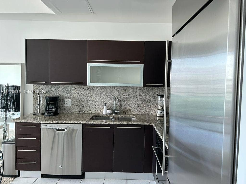 950 Brickell Bay Drive, #5108, Miami, Miami, FL 33131 Kitchen featuring dark-finish cabinetry, stone countertop, stainless steel dishwasher, integrated stainless steel refrigerator, and undermount dual-basin sink with metallic faucet